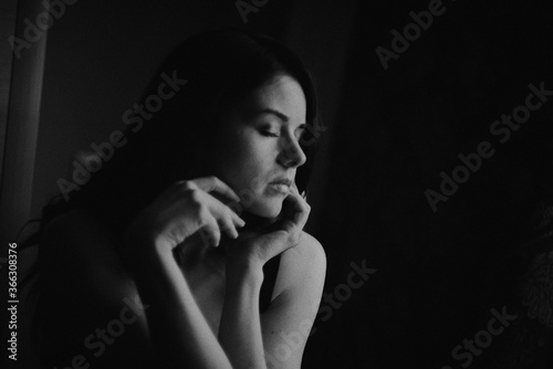 A girl with black hair in black underwear sits on a chair by the window