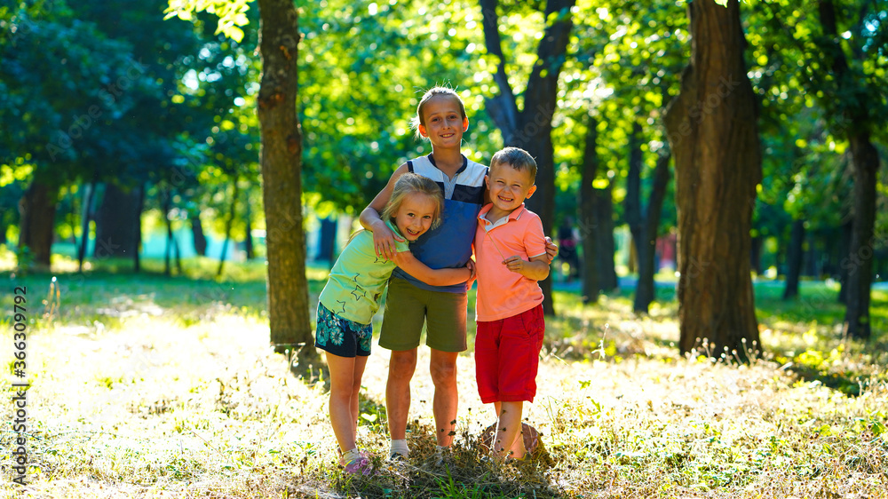 Three happy kids, little girl and two boys on lawn in the park