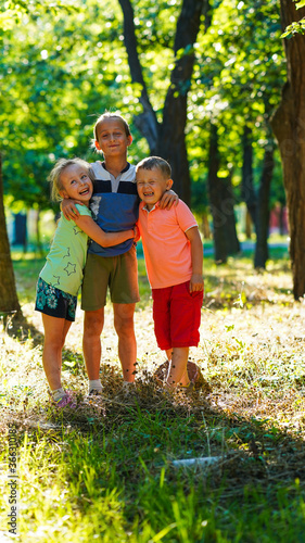 Three happy kids, little girl and two boys on lawn in the park