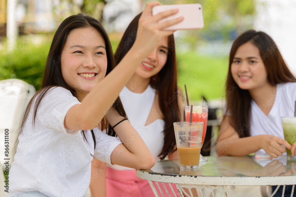Three happy young Asian women as friends taking selfie together at the coffee shop outdoors