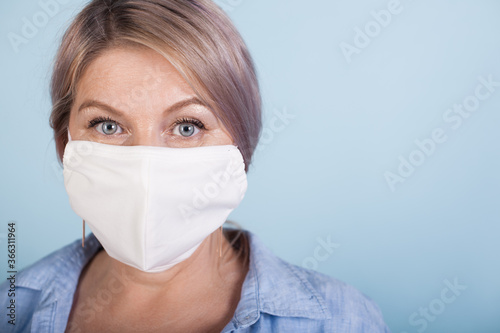 Close up photo of a caucasian woman with blonde hair wearing a medical mask on blue studio wall with free space
