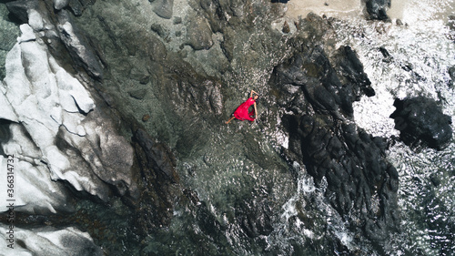Aerial photo: a charming lady lies among the rocks in a red dress