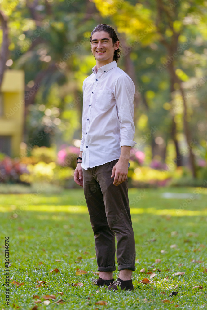 Full body shot of happy young handsome businessman smiling at the park outdoors