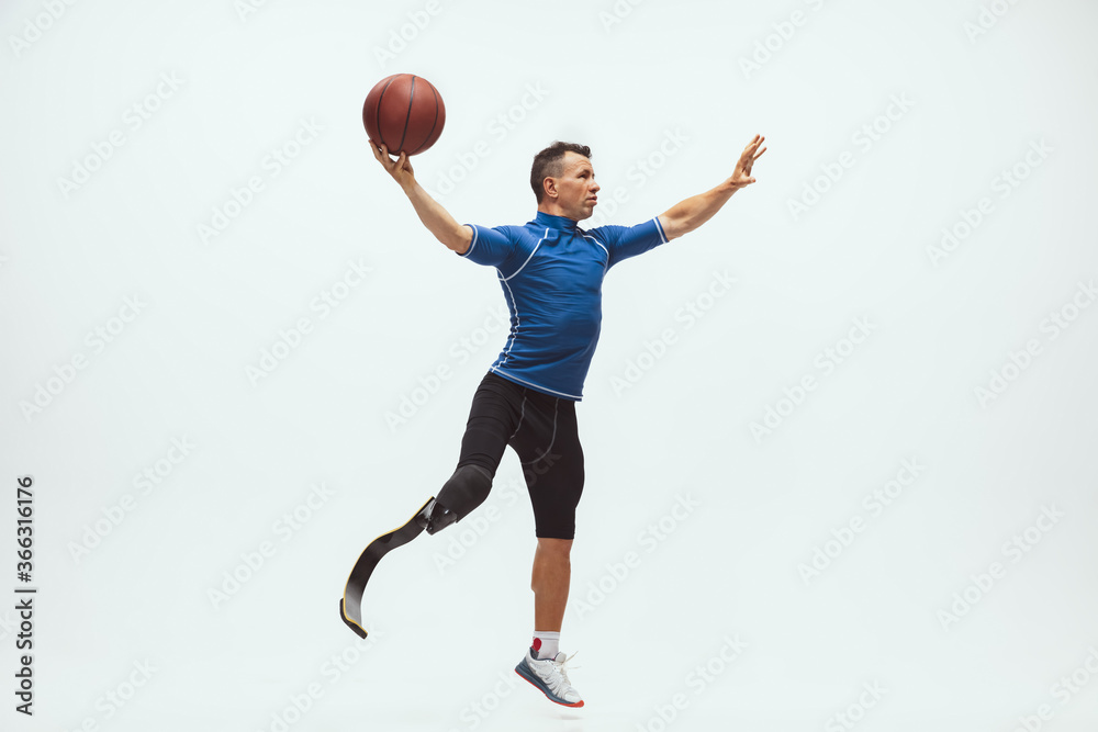 Athlete with disabilities or amputee on white studio background. Professional male basketball player with leg prosthesis training in studio. Disabled sport and healthy lifestyle concept. Achievements.