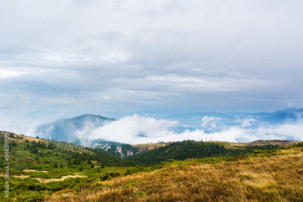 Valley with low clouds on Dragobrat. Landscape, foggy hills, forest in autumn. Daylight. Sun in the sky. Blue and blue colors. Resort in the forest.