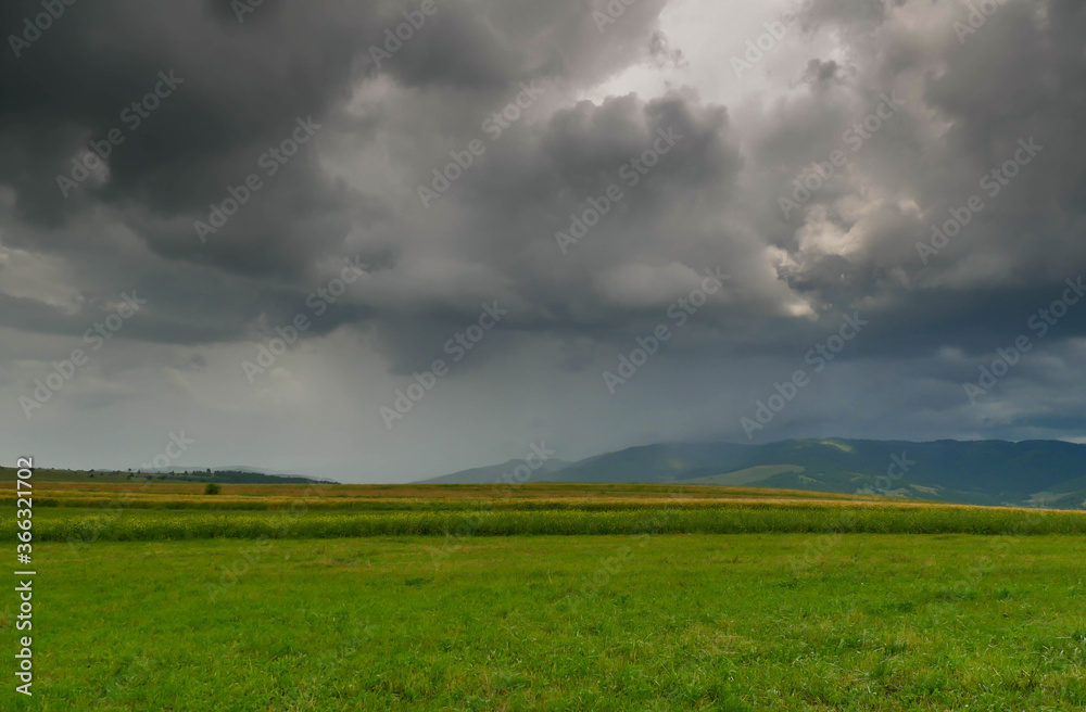 Dramatic stormclouds over green meadow at sunset in the Carpathian mountains, Romania.