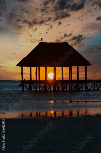 Pier over Caribbean Ocean at sunset, a little bird in the top of the hut, reflections on the water of the Caribbean Sea, Holbox, Mexico