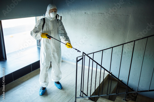 Sanitizing worker cleaning up the staircase at the shopping mall with an antiseptic to prevent covid-19 spread. A man in a disinfection suit sprays stairs. Healthcare, quarantine and hygiene concept. © Konstantin Zibert