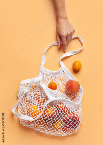 Peaches in a reusable shopping bag on an orange background.