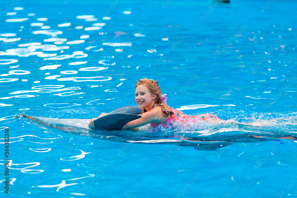 Happy little girl swimming with dolphins in Dolphinarium