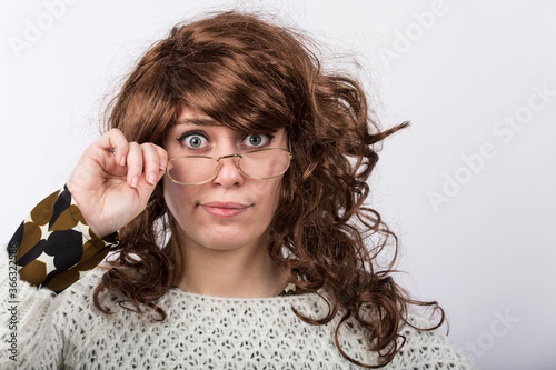Signora con capelli mossi castani e maglione sguarda con espressione molto severa e meravigliata toccandosi gli occhiali, isolata su sfondo bianco  photo