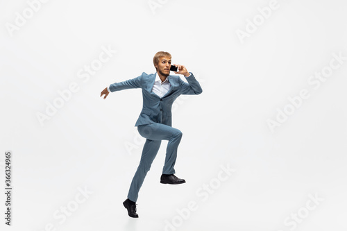 Talking on the go. Man in office clothes running, jogging on white background like professional athlete, sportsman. Unusual look for businessman in motion, action with ball. Sport, healthy lifestyle