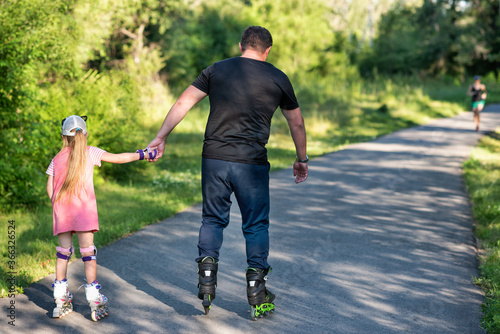 A father teaching his daughter roller skating in a park on summer day. Happy week-end. Father's day.