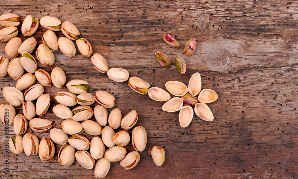Composition in the shape of a flower of the fruits of the pistacia vera, dry roasted pistachios on wooden background.