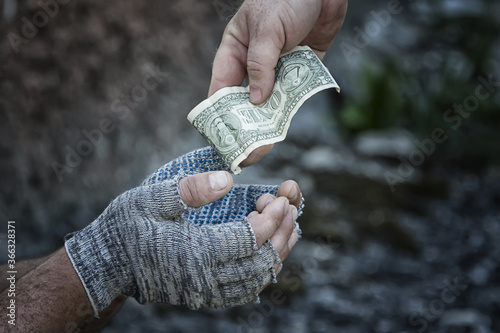 The hand of a passer-by gives a dollar to the hands of a homeless man in gloves. Poverty, hunger, unemployment.