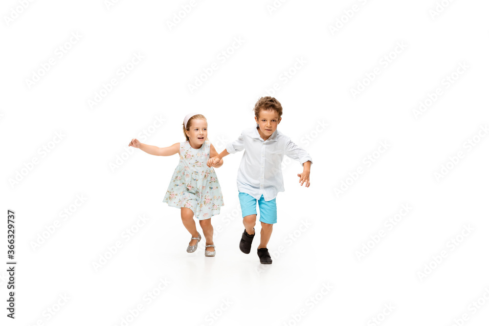 Happy children, little and emotional caucasian boy and girl jumping and running isolated on white background. Look happy, cheerful, sincere. Copyspace for ad. Childhood, education, happiness concept.