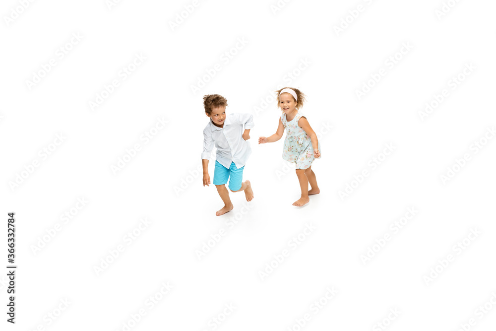 Happy children, little and emotional caucasian boy and girl jumping and running isolated on white background. Look happy, cheerful, sincere. Copyspace for ad. Childhood, education, happiness concept.