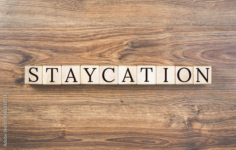 Staycation text on building blocks and wooden rustic background. New normal vacation during pandemic. Stay at home for vacation or holiday. Local neighborhood travel. Copy space