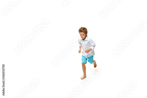 Happy child, little and emotional caucasian boy jumping and running isolated on white background. Looks happy, cheerful, sincere. Copyspace for ad. Childhood, education, happiness concept.