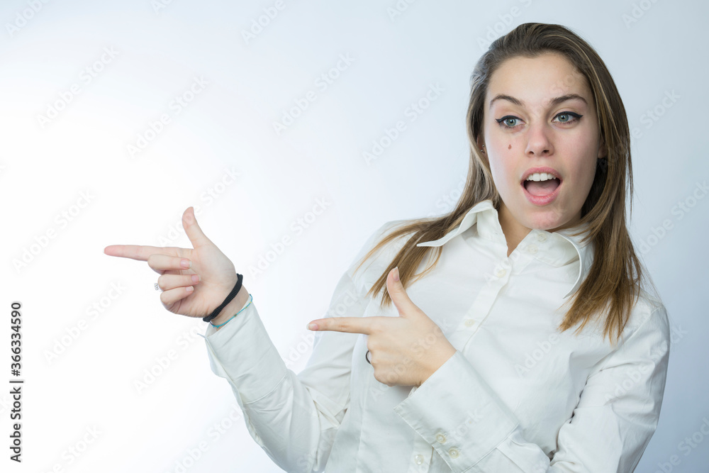 ragazza bionda con camicia bianca indica con aria stupita, isolata su sfondo chiaro ragazza bionda con camicia bianca indica con aria stupita, isolata su sfondo chiaro