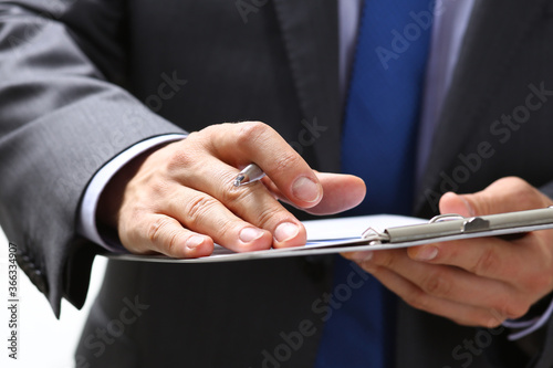 Focused photo on pad that being in male hands, attentive businessman making notes while listening to conference