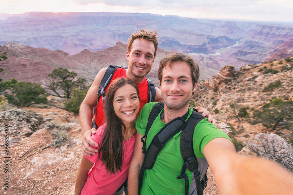 Selfie group of tourists friends hikers hiking outdoor. Happy people taking self portrait photo together in Grand Canyon nature park travel vacation. Group of three : Asian woman, two young man.