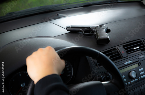 Theft of the car. Man with gun behind the wheel. Carjacking of vehicle. Robbing and crime. © Vadym