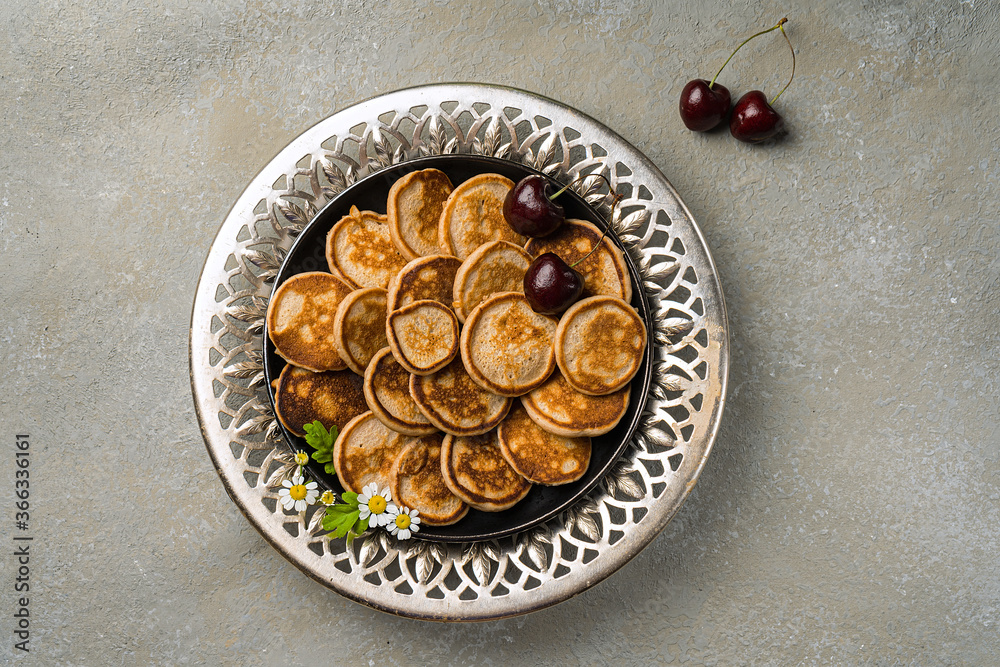 A trendy homemade breakfast with tiny pancakes close-up. Mini pancakes, cherries, tea on the table in an openwork plate A trendy homemade breakfast with tiny pancakes close-up. Mini pancakes, cherries, tea on the table in an openwork plate
