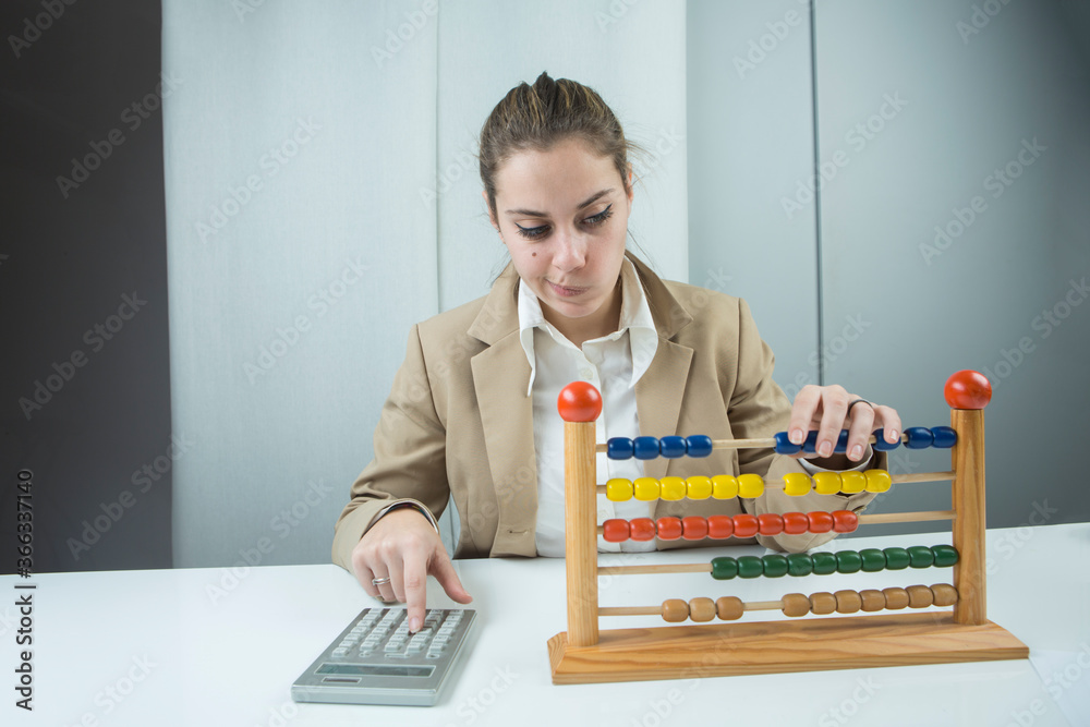 ragazza bionda vestita con una giacca beige è seduta nella sua postazione di lavoro , mentre cerca di fare dei conti con un pallottoliere colorato ragazza bionda vestita con una giacca beige è seduta nella sua postazione di lavoro , mentre cerca di fare dei conti con un pallottoliere colorato