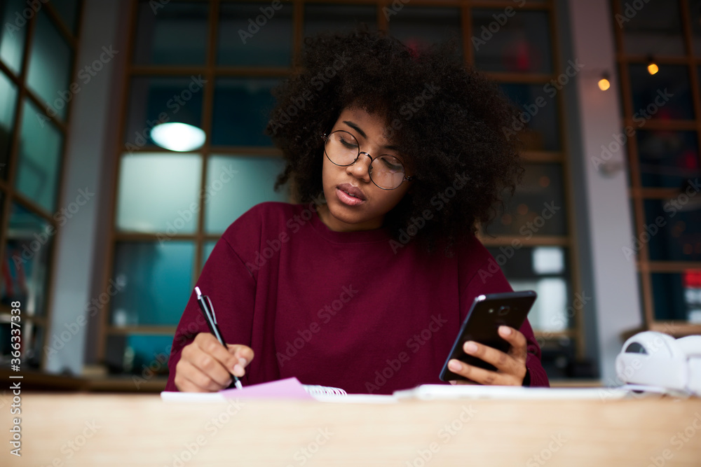 Afro american student sitting at table in university campus looking into camera holding modern smartphone