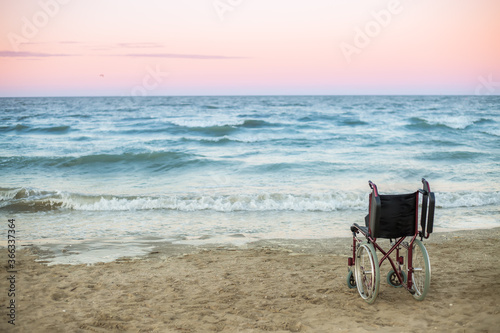 One wheelchair for disabled people stands by the sea at sunset