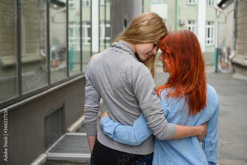 Same-sex relationships. A happy lesbian couple walked along the street and gently hug each other around the waist. The backs of two beautiful women on a date with a bouquet of dried flowers. LGBT.