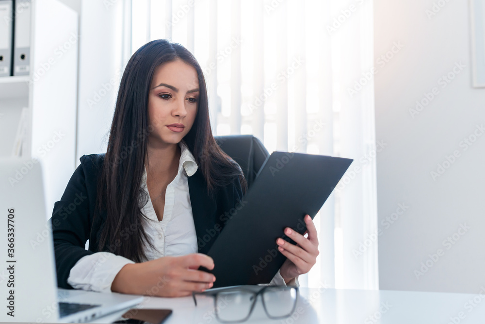 Young business woman sitting in office and looking at clipboard. Young business woman sitting in office and looking at clipboard.
