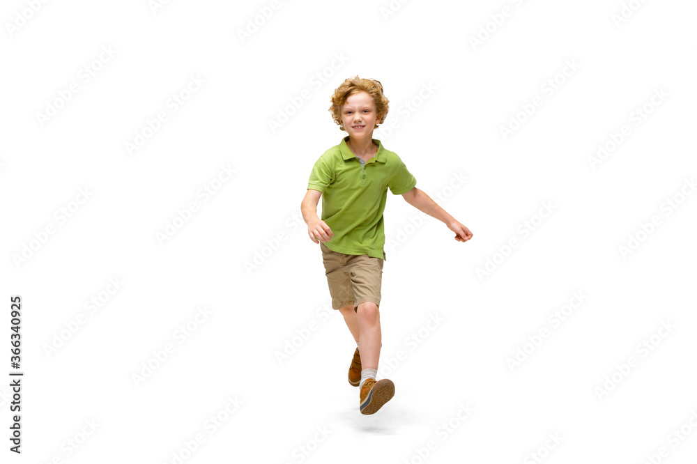 Happy child, little and emotional caucasian boy jumping and running isolated on white background. Looks happy, cheerful, sincere. Copyspace for ad. Childhood, education, happiness concept.