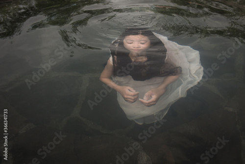 Girl in white dress swimming under water towards surface