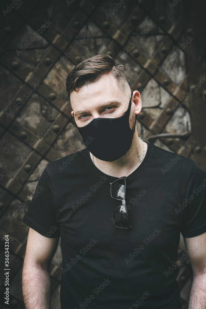 Handsome brutal man in a black T-shirt and a fashionable black protective face mask. A man is looking at the camera. Outdoors. Handsome brutal man in a black T-shirt and a fashionable black protective face mask. A man is looking at the camera. Outdoors.