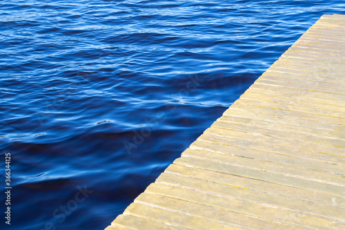 Water texture. Copy space, place for text. Empty wooden pier and blue water surface with small waves. High angle view to lake, sea or river.