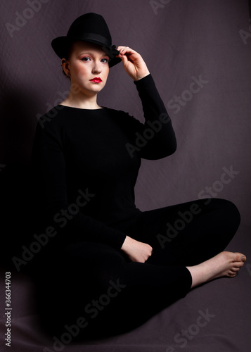 Young woman in heavy make up wearing a black hat. In low key lighting.
