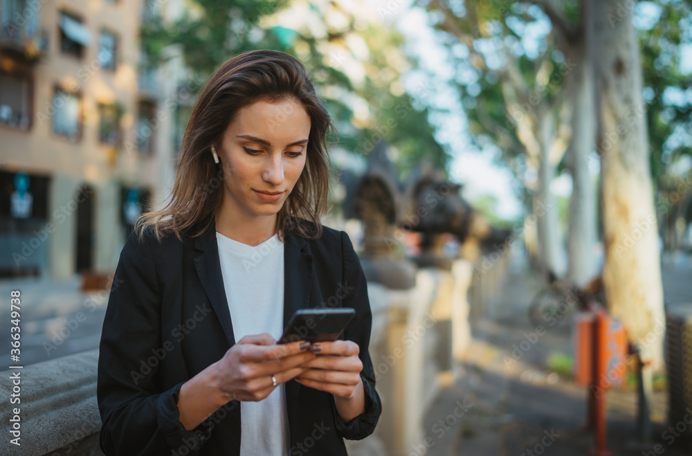 Cheerful businesswoman in jacket with cell phone in park, portrait elegant woman with smartphone and wireless earphones on street city, business woman using phone outdoors