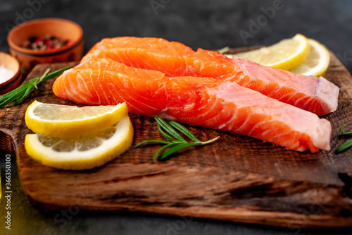 pieces of raw salmon with spices and lemon on a stone background