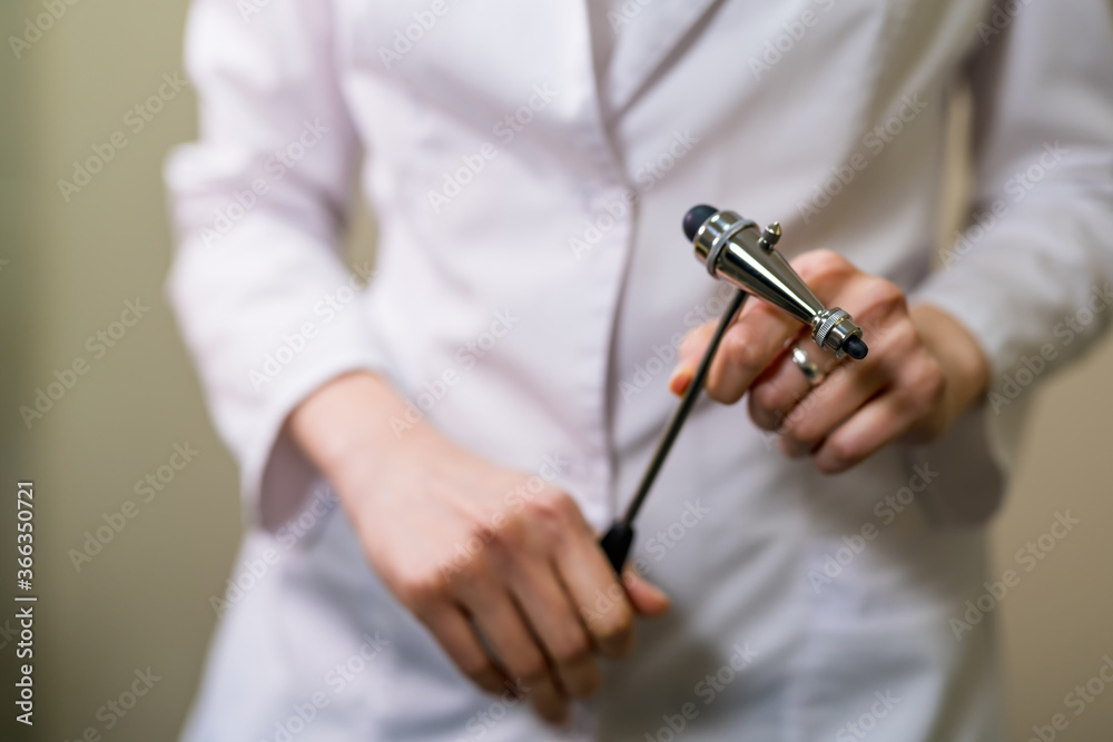 Doctor holding reflex hammer toward camera, focus on the foreground, on the hammer.