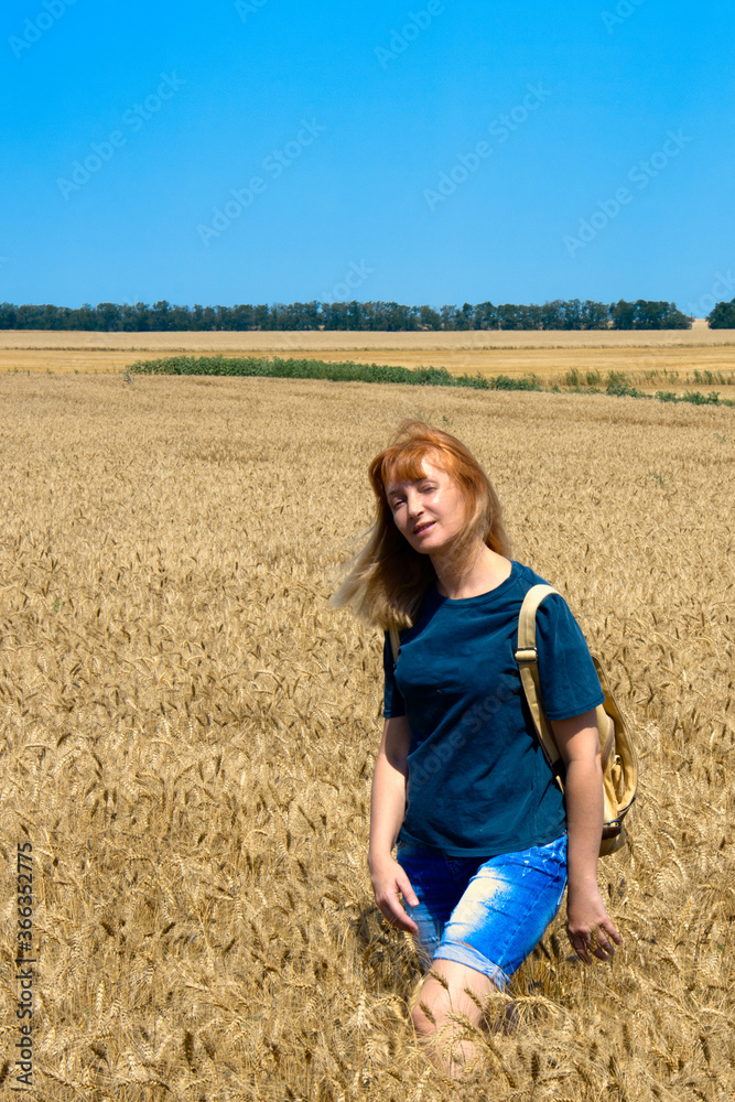 A young woman walks through a golden wheat field. Summer sunny day, the sun is shining brightly. Healthy lifestyle. Good mood A young woman walks through a golden wheat field. Summer sunny day, the sun is shining brightly. Healthy lifestyle. Good mood