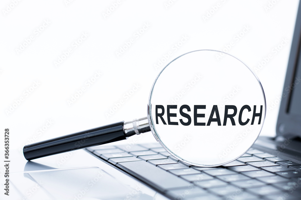 magnifier with the inscription Research lies on the laptop keyboard. magnifier with the inscription Research lies on the laptop keyboard.