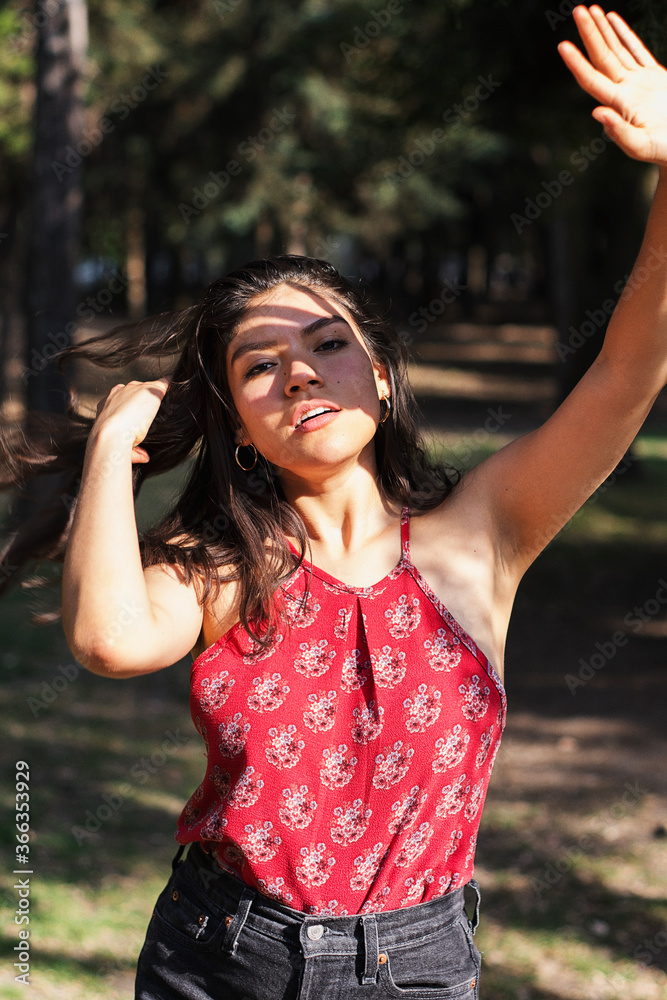 Medium shot portrait of a beautiful young lady in park. Sunlight hitting her face while the shadow of her hand reflects in her face
