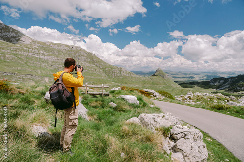travel photographer in mountains. Professional photographer travel in countryside with camera and taking photos. tourist male with backpack on summer vacations. Montenegro, Durmitor. 
