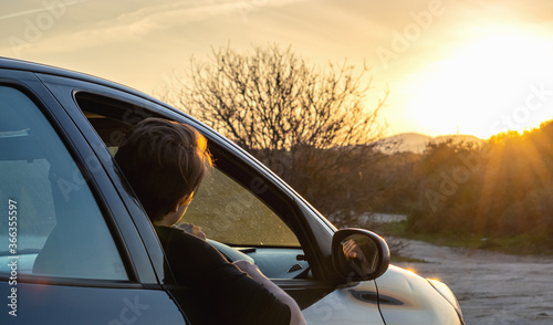 Young man sitting in car and looking at beautiful sunset