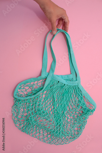 Womens hand takes cotton green mesh bag on pink paper background. Eco-friendly shopping without plastic