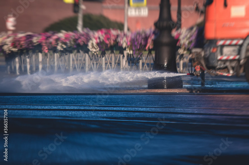 Cleaning flusher sweeper machines washes the city streets road with water spray, group of municipal watering machines wash asphalt, process of street disinfection and cleaning from dust and dirt photo