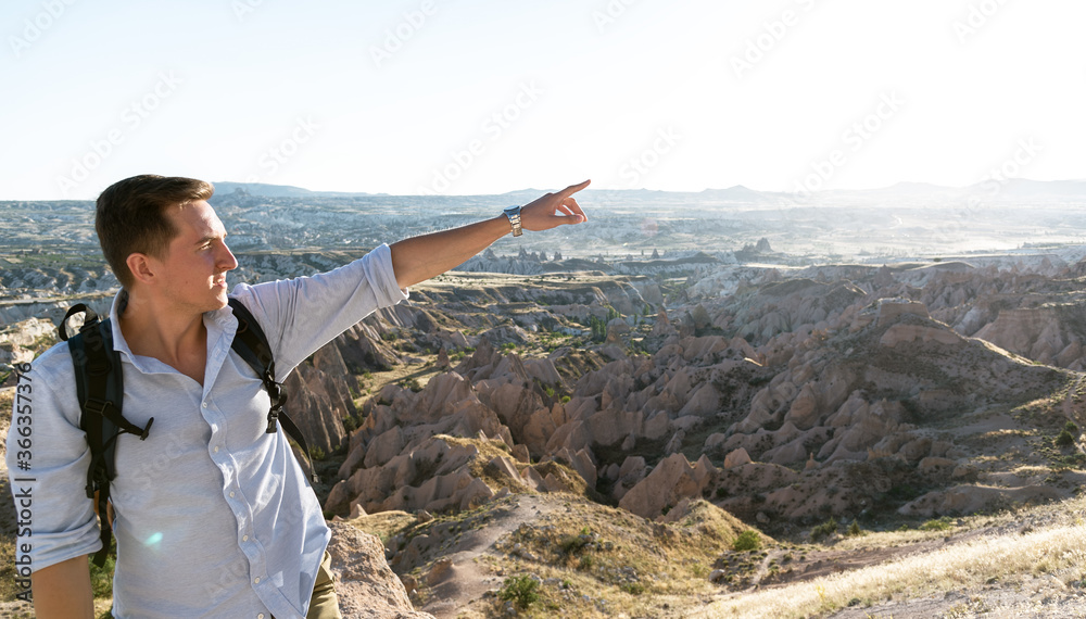 Young man with backpack standing against beautiful valley at Cappadocia. Copy space. Bleisure concept