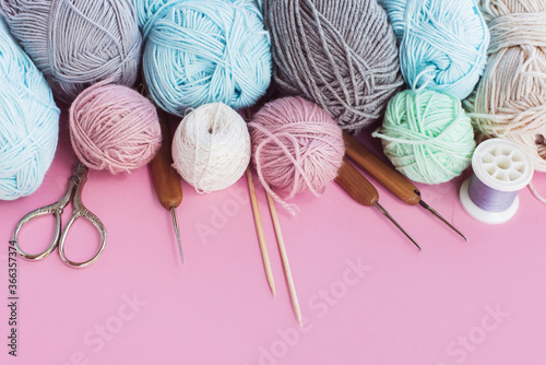 Women's hobby. Multicolored skeins, needles, hooks on the pink background. Conept of sewing, crochet and knitting. 
